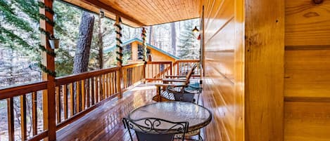 Una cabaña de madera con una terraza panorámica que incluye una mesa redonda y sillas, rodeada de barandillas de madera y grandes ventanales.