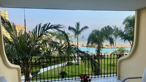 Un balcon avec vue sur une piscine, des palmiers et un bâtiment situé au loin.