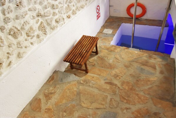 A wooden bench against a white wall with a stone floor, a lifebuoy, and a blue-lit area in the background.