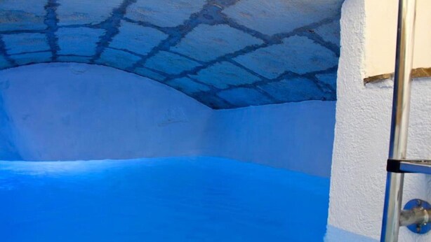 Une pièce dont le plafond et les murs sont peints en bleu, avec une échelle appuyée contre le mur et une porte blanche.