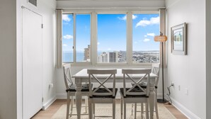 Ein Essbereich mit Tisch und Stühlen, ein Fenster mit Blick auf die Stadt und einer hängenden Leuchte.