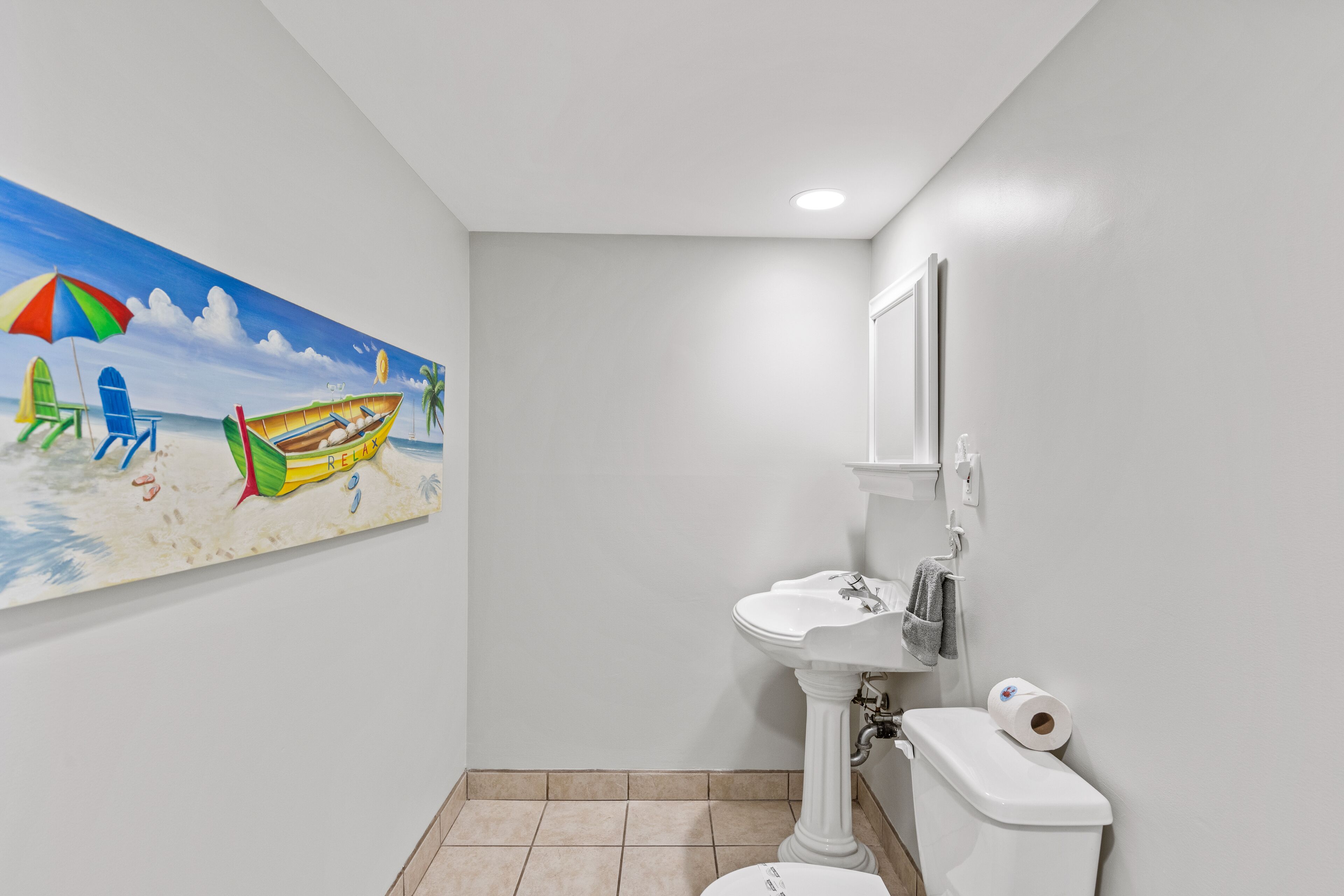 Casa de banho com um mural com tema praiano, uma pia assentada e uma sanita.