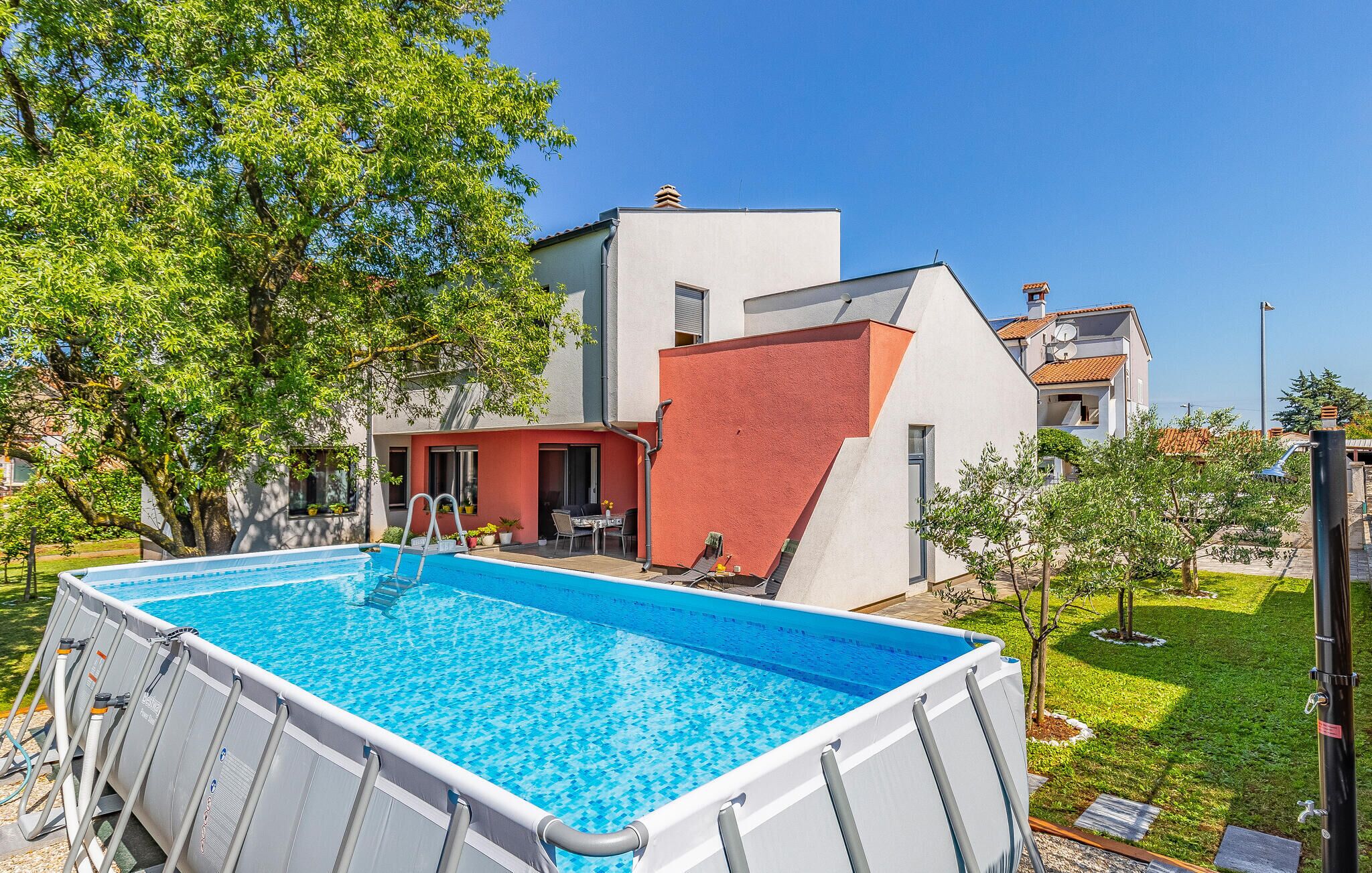 A swimming pool with a ladder, surrounded by a grassy area and trees.