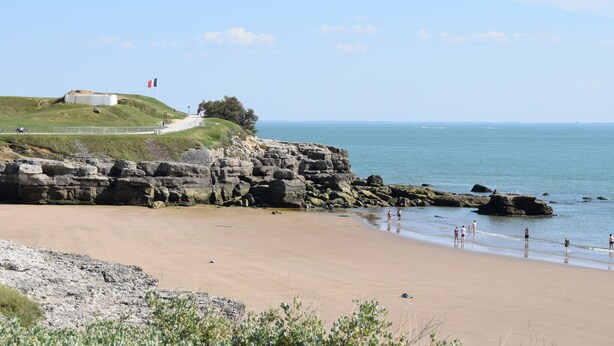 Un paysage côtier avec une colline herbeuse, une côte rocheuse et une vue dégagée sur la mer.