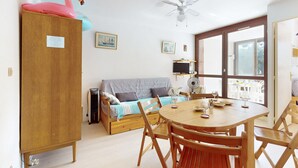 Une pièce chaleureuse avec une armoire en bois, un lit recouvert d’une couverture à rayures bleues et blanches, une table à manger avec des chaises en bois et un ventilateur de plafond.
