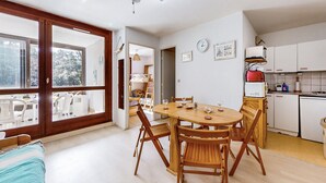 Une cuisine compacte avec des meubles blancs, une table à manger entourée de chaises en bois et une grande fenêtre donnant sur la verdure.