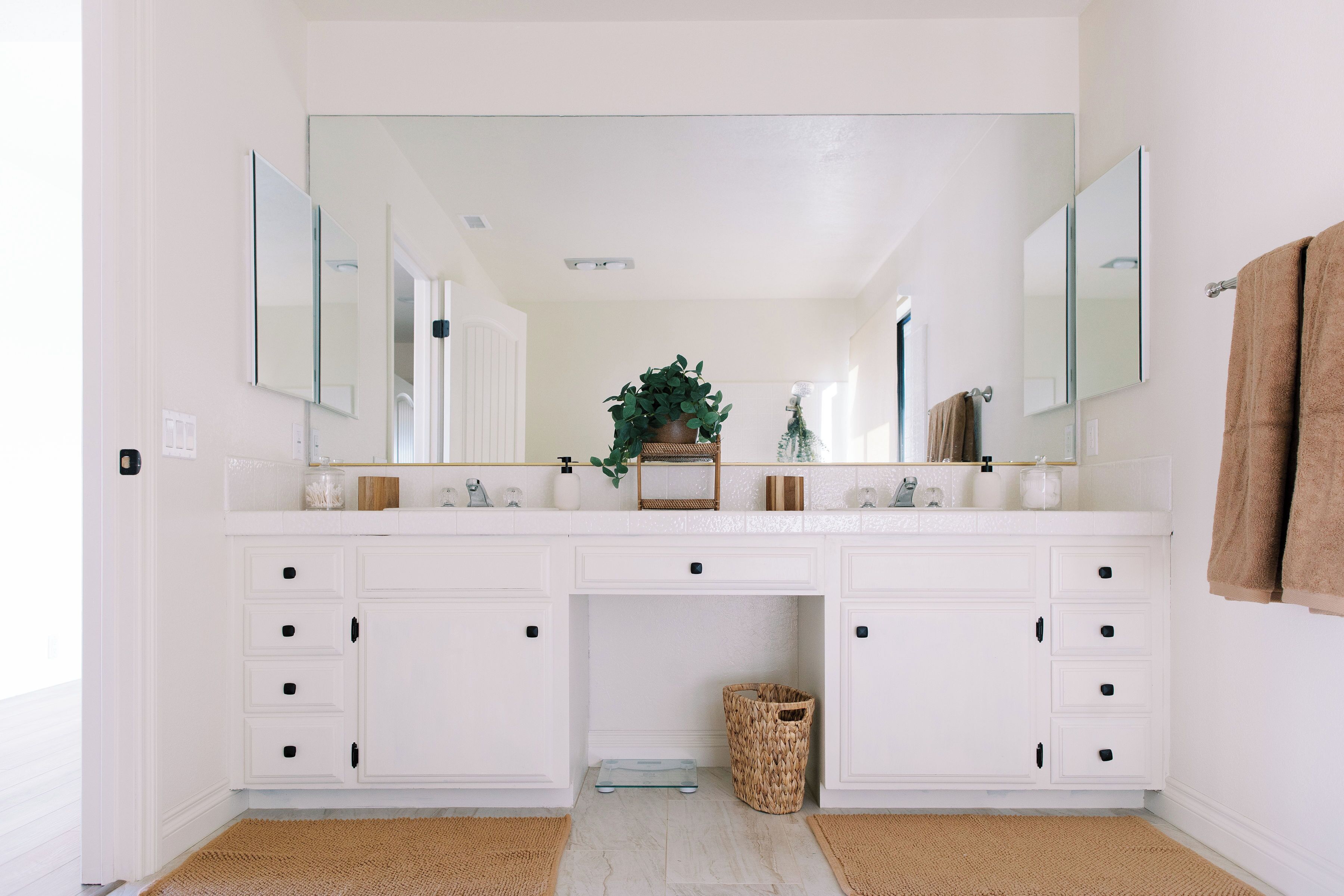 A bathroom with white cabinetry, a large mirror, and a plant on the vanity.