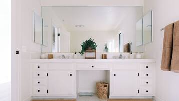 A bathroom with white cabinetry, a large mirror, and a plant on the vanity.