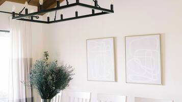 A dining area with a wooden ceiling, a chandelier, a white dining table, and two framed abstract artworks on the wall.