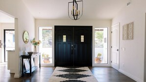 A hallway with a dark wooden door, a black and white rug, a table with a lamp, and a mirror. - Luxury Retreat, views of Monserate Winery (San Diego County)