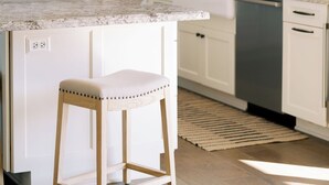 A modern kitchen with white cabinets, a granite countertop, a wooden stool, and a built-in dishwasher. - Luxury Retreat, views of Monserate Winery (San Diego County)