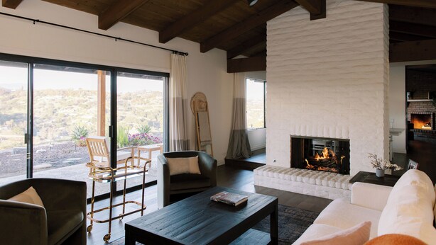 A modern living room with a fireplace, large windows, and a view of the outdoors. - Luxury Retreat, views of Monserate Winery (San Diego County)