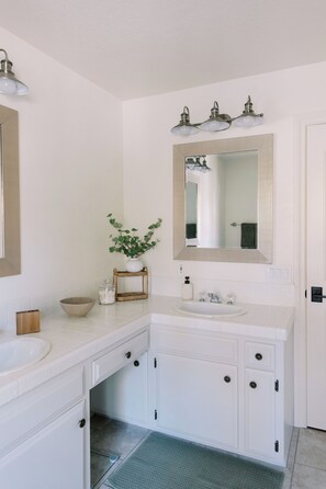 A bathroom with a white sink, mirror, and cabinets. There is a plant on the counter and a small wooden tray. - Luxury Retreat, views of Monserate Winery (San Diego County)