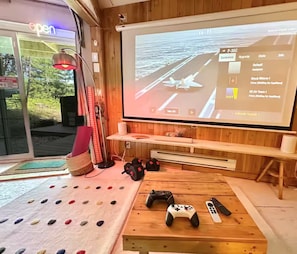 A gaming setup with a large screen, a wooden table, and gaming accessories.