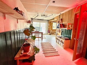 A hallway with a pegboard wall, a wooden table with a potted plant, and a red-lit door.