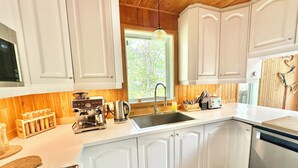 A kitchen with white cabinets, a coffee machine, a sink, and a window with a view of trees. - Adventures On the lake / boat, cinema, spa, trails (Chute-Saint-Philippe)