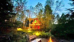 A cabin surrounded by trees with a fire pit and a bench in the foreground. - Adventures On the lake / boat, cinema, spa, trails (Chute-Saint-Philippe)