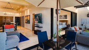 A modern living room with a large umbrella, a dining area, and a bedroom with a bed and nightstands.