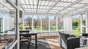 A sunroom with a wooden floor, a dining table with chairs, and a view of a garden. - 3 bedroom stunning home in Højby (Højby)