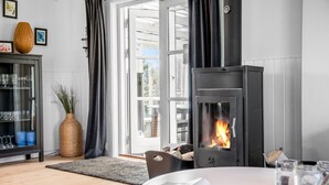 A modern living room with a wood-burning stove, a glass cabinet with decorative items, and a view through large glass doors. - 3 bedroom stunning home in Højby (Højby)