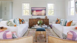 A living room with white sofas, a wooden coffee table, and a flat-screen TV mounted on the wall. - Chic Shellter, Bald Head Island, NC (Bald Head Island)
