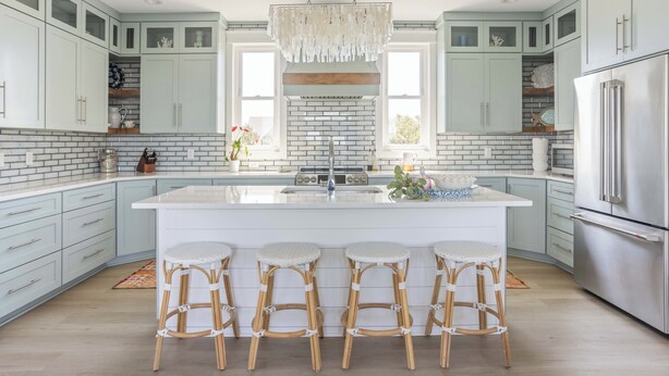 A modern kitchen with light blue cabinets, a white island with bar stools, a brick backsplash, and stainless steel appliances. - Chic Shellter, Bald Head Island, NC (Bald Head Island)
