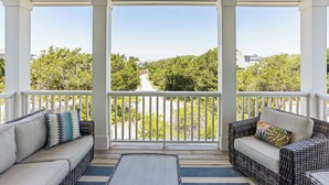 A covered porch with two wicker sofas and a view of a tree-lined road. - Chic Shellter, Bald Head Island, NC (Bald Head Island)