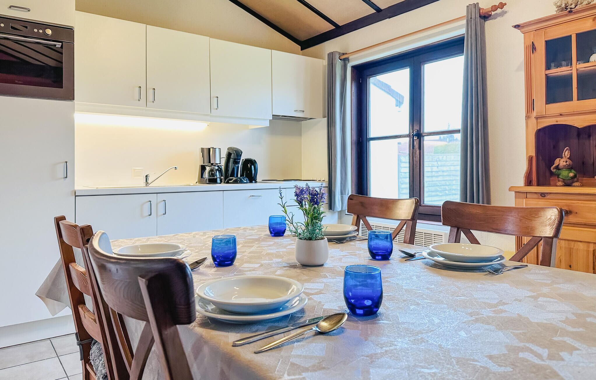 Een moderne keuken met witte kasten, een inbouwoven en een eethoek met een tafel gedekt voor twee personen.