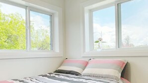 Un dormitorio con cama, dos ventanas y vistas a árboles.