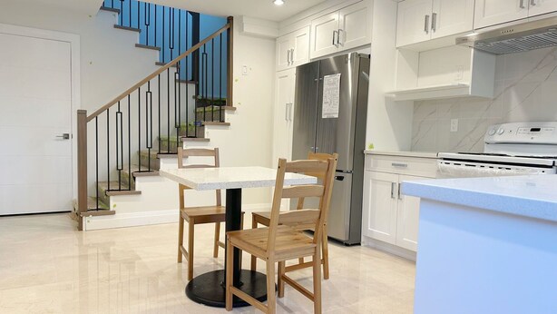 Una cocina moderna con armarios blancos, un refrigerador de acero inoxidable, un horno empotrado y una zona de comedor con mesa y sillas.