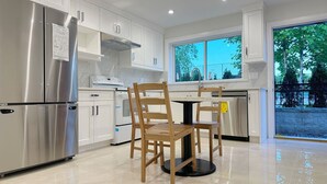 Una cocina moderna con armarios blancos, electrodomésticos de acero inoxidable y un comedor con sillas de madera.