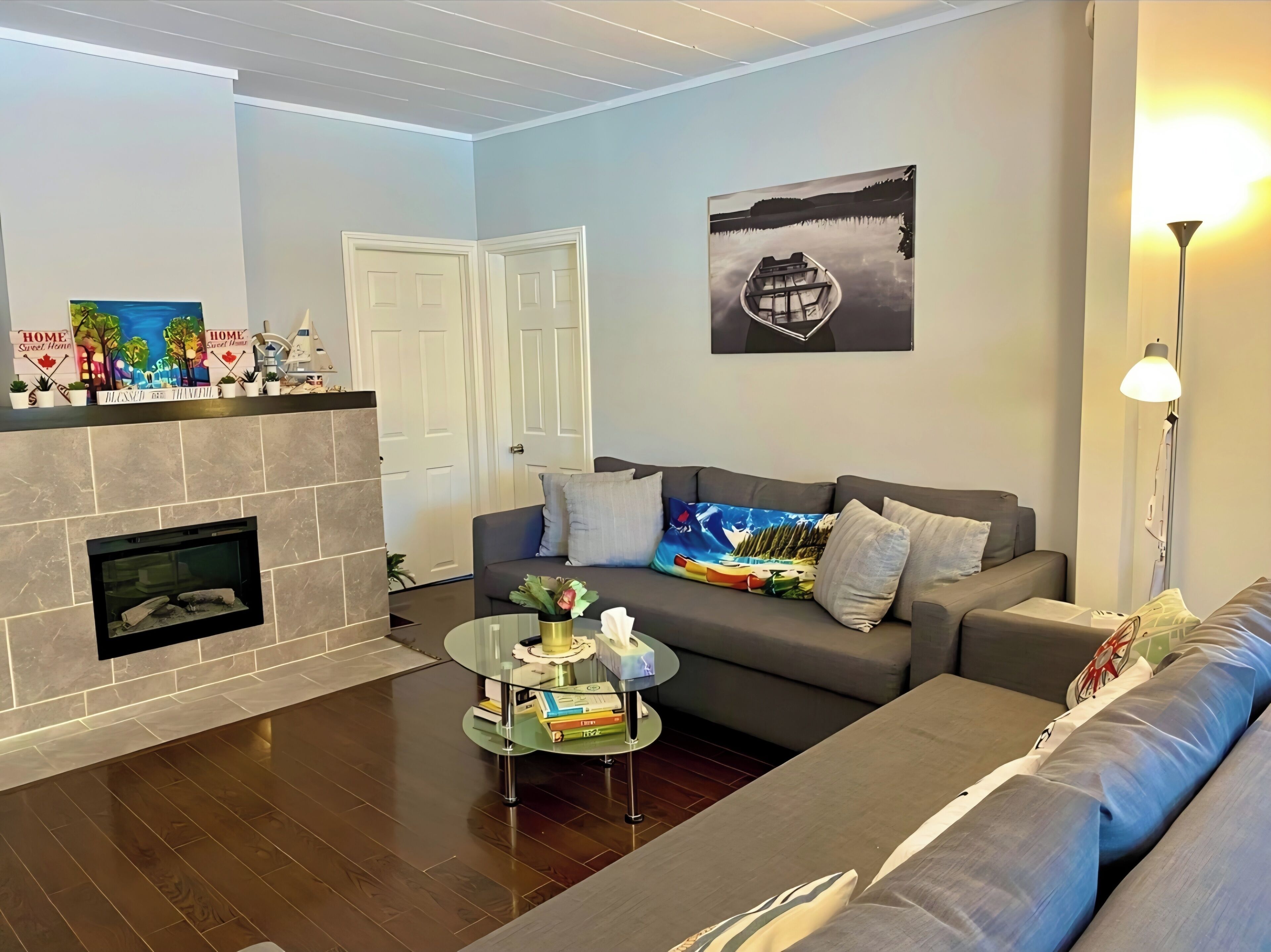 A living room with a fireplace, a sofa, a coffee table with books, and a painting on the wall.