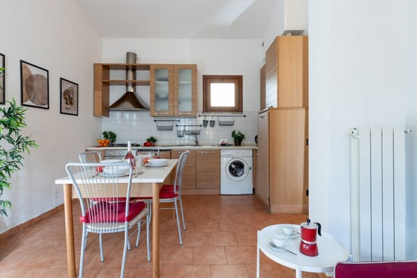 A compact kitchen with a dining area, a washing machine, and a small table with a coffee maker.