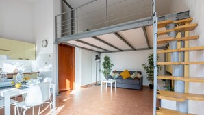 A modern kitchen with white cabinets, a dining table with chairs, a sofa with cushions, and a staircase with wooden steps. - GuestHost - Cozy studio apartment of about 50 sqm with mezzanine, located on the ground floor (one step at the entrance), able to comfortably accommodate up to 4 people. The accommodation is located in a quiet neighborhood, with all the main services. Wi (Pisa)
