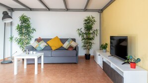 A living room with a sofa, a coffee table, a TV, and two potted plants. - GuestHost - Cozy studio apartment of about 50 sqm with mezzanine, located on the ground floor (one step at the entrance), able to comfortably accommodate up to 4 people. The accommodation is located in a quiet neighborhood, with all the main services. Wi (Pisa)