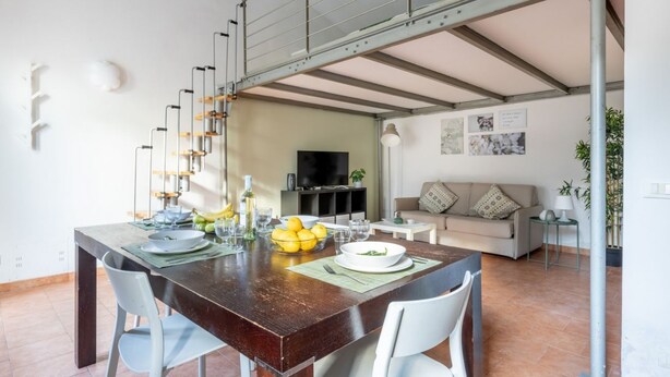 A dining area with a wooden table, white chairs, and a TV in the background. - GuestHost - Cozy studio apartment of about 50 sqm with mezzanine, located on the ground floor (one step at the entrance), able to comfortably accommodate up to 4 people. The accommodation is located in a quiet neighborhood, with all the main services. Wi (Pisa)