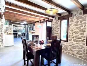 A dining area with a stone wall, wooden ceiling beams, and a table set for four.