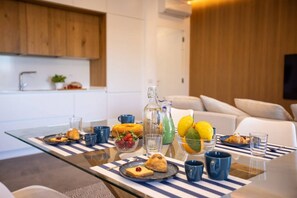 A modern kitchen with a glass table set for breakfast, featuring pastries, fruits, and beverages. - Modern Family Apt in Sorrento with Views (Sorrento)