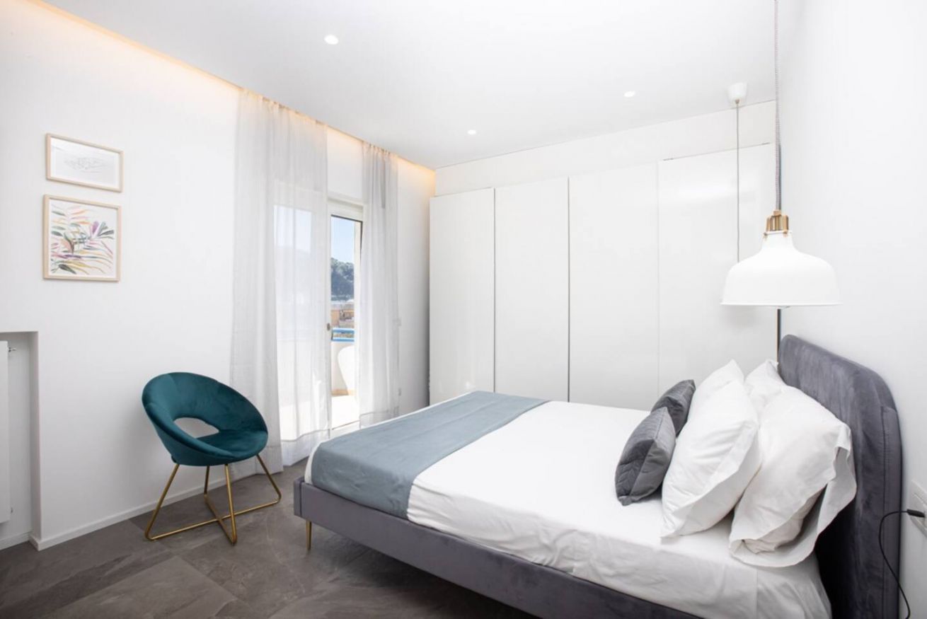 A modern bedroom with a bed, a chair, and a window with curtains.