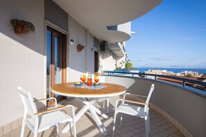 Uma varanda com uma mesa de madeira redonda e cadeiras brancas, com vista para a costa.