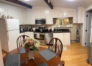 A modern kitchen with white cabinets, stainless steel appliances, and a dining area with a wooden table and chairs.