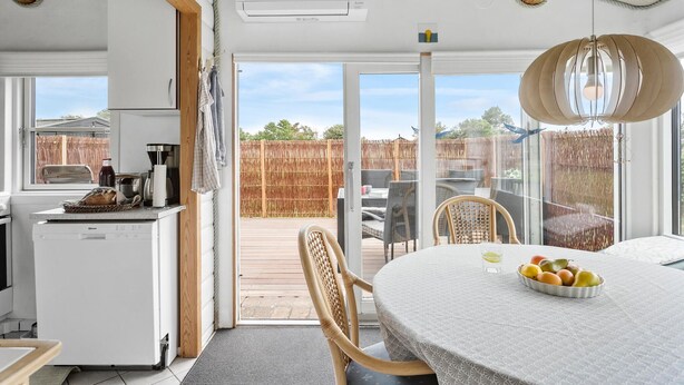 A kitchen with a refrigerator, a coffee machine, and a dining area with a table and chairs. - 2 bedroom gorgeous home in Nakskov (Nakskov)