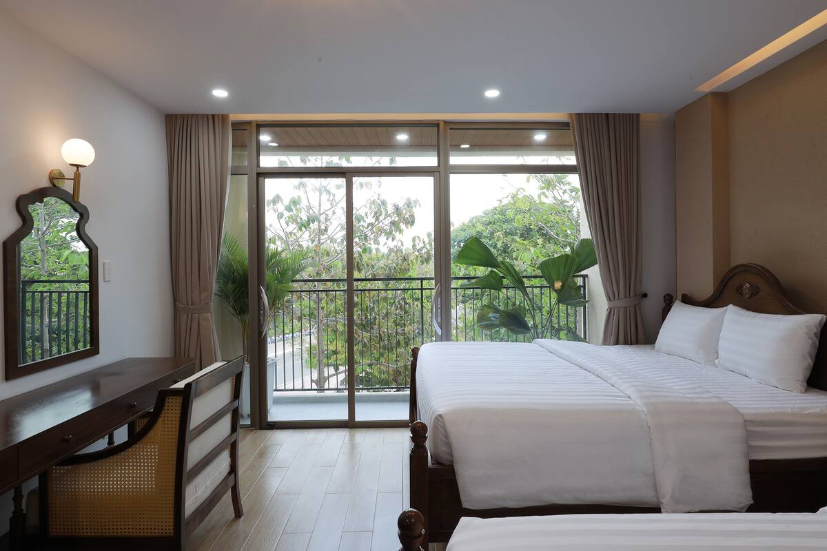 A hotel room with a large bed, a desk, and a balcony with a view of greenery.