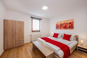 Ein Schlafzimmer mit Bett, Nachttisch, einem Fenster mit Jalousien, einer Heizung und einem Kleiderschrank.