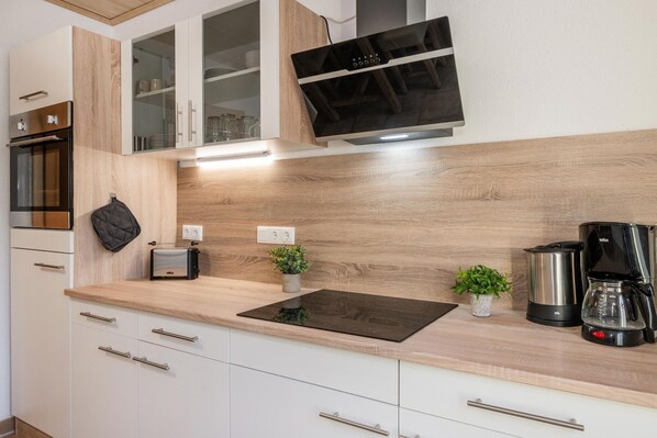 A modern kitchen with white cabinets, a built-in oven, a microwave, a toaster, a coffee maker, and a small potted plant.