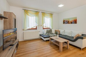 Een moderne woonkamer met een bank, een salontafel en een televisie op een houten standaard.