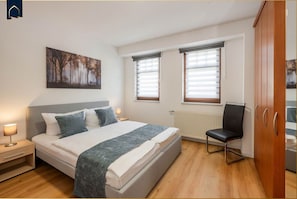A bedroom with a bed, bedside table, lamp, and a chair.