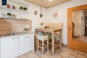 A compact kitchen with a wooden countertop, white cabinets, and a sink. There is a small table with two chairs and a vase of flowers.