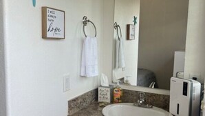 A bathroom with a white sink, wooden cabinets, a large mirror, and a towel rack. - Rogue River Landing #31A (Gold Beach)