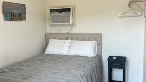 A bedroom with a bed, an air conditioning unit, a small bedside table, and a wall-mounted air conditioner. - Rogue River Landing #31A (Gold Beach)